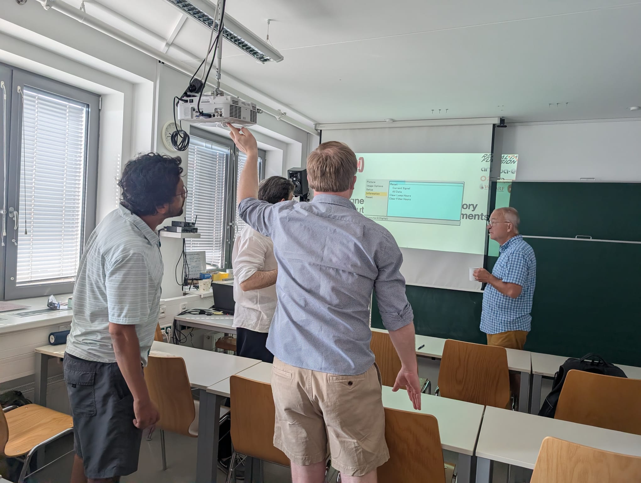 Several physicists gathered beneath a ceiling-mounted projector, trying to get it working
